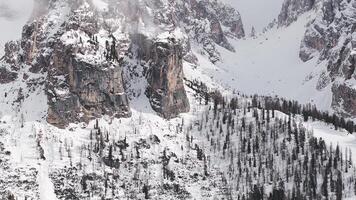 Aerial view of misty Dolomite mountains near Cortina, with rugged peaks, snowy cliffs, and scattered evergreen trees in a serene winter setting. video