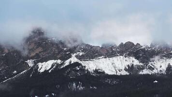 Aerial view of rugged Dolomite mountains near Cortina with snow dusted peaks, mist, and low clouds. Slow pan highlights light and shadow interplay. video
