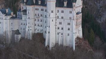 Aerial view of Neuschwanstein Castle at sunset, showcasing its spires and tower. Rugged cliffs, dense forest, and a distant church complete the scene. video
