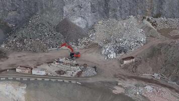 Aerial view of a mining site in the Alps showing an orange excavator moving debris, rugged terrain, dirt roads, and scattered industrial structures. video