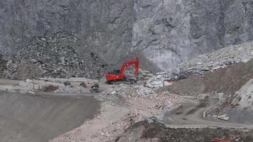 Aerial view of a mining site in the Alps with a red excavator moving debris near rubble piles, surrounded by dirt roads and rugged terrain. video