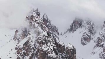 Aerial view of rugged, snow covered Dolomite peaks near Cortina, with mist and clouds drifting over cliffs and scattered evergreen trees. video