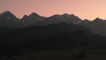 Antenne Aussicht von neuschwanstein Schloss im Bayern, Deutschland, beim Sonnenuntergang. beleuchtet Schloss mit Berg Hintergrund, Wicklung Straße, und Dorf Beleuchtung sichtbar. video
