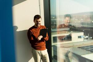 A man is standing in front of a window with a tablet photo