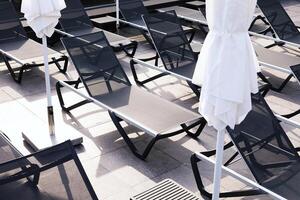 Modern sun loungers and closed umbrellas on a resort terrace, arranged in geometric patterns with sunlight and shadows photo