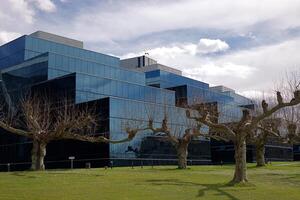Modern glass office building reflecting sky and clouds, with knobby leafless trees in the foreground. photo
