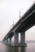 Large concrete bridge spanning a wide river on an overcast day. The perspective emphasizes the structure's scale and architectural details. photo