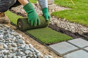 Laying Down Artificial Turf in a Garden Pathway During a Sunny Afternoon in a Residential Yard photo