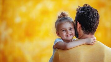 Father and Daughter Share a Joyful Moment Against a Vibrant Yellow Background During Golden Hour photo
