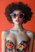 Woman in Colorful Swimsuit and Sunglasses Poses Against Bright Orange Background photo