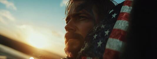 Courageous Soldier Gazes Into the Sunset While Wrapped in an American Flag by the Ocean photo