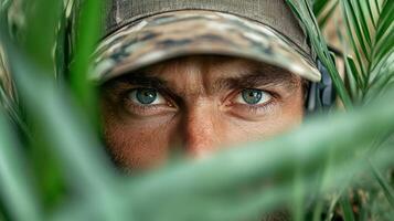 A man in camouflage is peeking out from behind the foliage photo