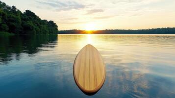 A wooden paddleboard sits on the water at sunset photo
