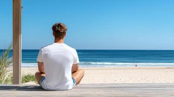 A man sitting on a wooden deck looking out to the ocean photo