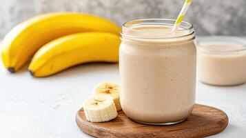 A jar of banana smoothie with a straw and bananas photo