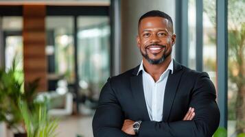 A smiling black man in a suit standing in front of a window photo
