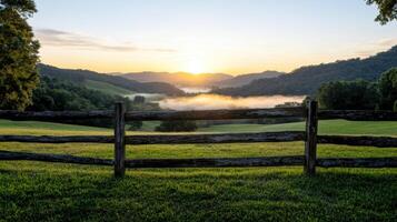 A fence in a field with a sunrise over the mountains photo