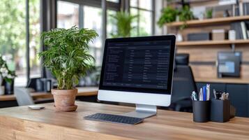 A desktop computer is sitting on a wooden desk with a plant and a pen photo