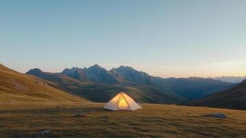 A tent is set up on a grassy hill with mountains in the background photo