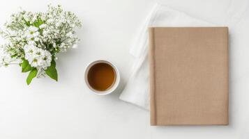 cozy scene featuring linen covered book, cup of tea, and bouquet of white flowers marble surface photo