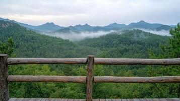 Breathtaking view of misty mountains and lush greenery from wooden terrace at dawn photo