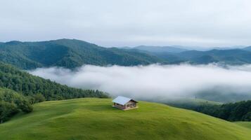 A small house on a hill in the middle of a green valley with fog photo