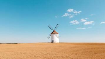 Old windmill on hill overlooking golden fields under clear blue sky photo