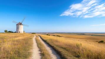 Old windmill on hill overlooking golden fields and blue sky creates serene landscape photo