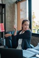 Professional woman in a modern office environment, taking a break and stretching by a large window with natural light. photo
