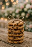 Beautifully Stacked Chocolate Chip Cookies Decorated With Twine on a Wooden Table in a Floral Setting photo