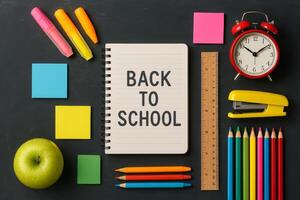 Back to School Supplies Arrangement With Colorful Stationery and an Apple on a Black Background photo