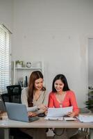 Two women working together at a home office desk, using a laptop and reviewing documents, creating a collaborative and productive atmosphere. photo