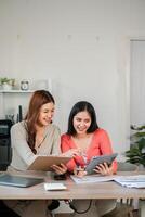 Two women working together in a modern office, using a tablet and documents for business planning and collaboration. photo