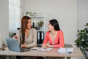 Two women working together at a desk, discussing ideas with a laptop and documents in a modern office setting. photo