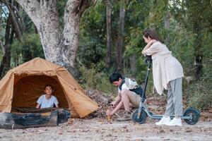 A family camping in the forest with a tent and scooters, enjoying nature and outdoor activities. photo