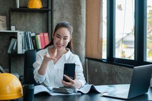 Smiling woman in white shirt using smartphone for call in a modern office setting with construction elements. photo