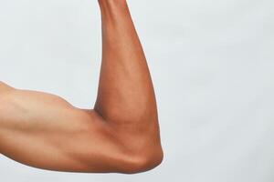 Closeup Of A Flexed Muscular Arm With Brown Skin Against A Light Background photo