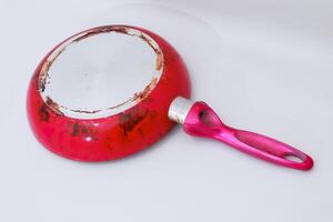Worn red skillet with metallic base and pink handle on plain background photo
