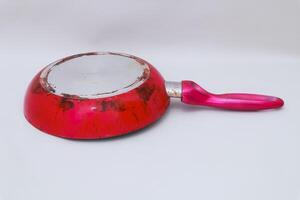 Well-Used Red Frying Pan with Pink Handle Resting on a White Surface photo
