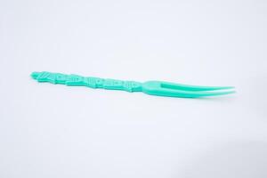 Close-up of bright turquoise color small fork on white smooth surface background photo