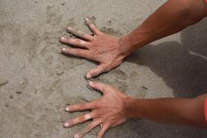 A man's palms press into the texture of the beach sand, making temporary marks photo