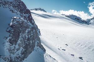 Snow covered rock face and smooth ski slopes in Zermatt, Switzerland. A structure atop a peak and a clear blue sky complete the winter scene. photo