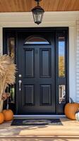 A black front door with pumpkins and a wreath photo