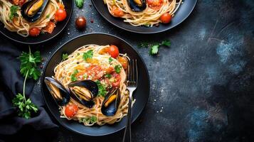 Spaghetti with mussels and tomatoes on black plates top view photo