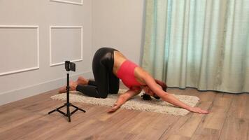 lady doing yoga lying on the floor at home and also broadcasting to her followers using a smartphone mounted on a tripod video