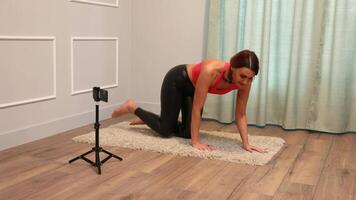 middle-aged lady doing yoga standing on the floor at home and also broadcasting to her followers using a smartphone mounted on a tripod video