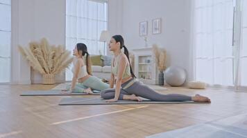 Two women are engaged in a yoga practice inside a spacious and bright living room. One woman is guiding the other, demonstrating a pose while providing support. video