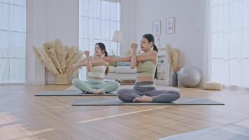 yoga practice inside a spacious and bright living room. One woman is guiding the other, demonstrating a pose while providing support. video