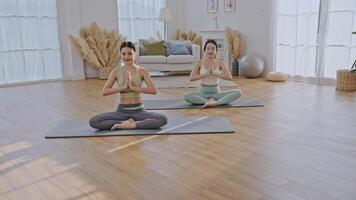 Two women in a yoga practice inside a spacious and bright living room. One woman is guiding the other, demonstrating a pose while providing support. video