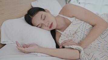 A woman rests in a serene bedroom, wrapped in a light blanket. She enjoys a peaceful sleep, with soft sunlight gently illuminating the room, creating atmosphere. video
